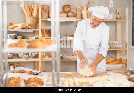 Senior man works in bakery as baker, kneads dough, works with flour. Stock Photo