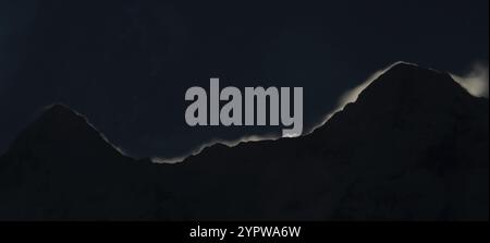 The famous Swiss peaks Eiger and Moench in interesting light, when the moon rises behind the mountains. Dark image with the silhouette of the peaks in Stock Photo