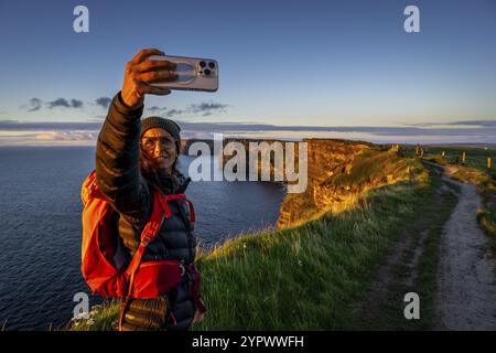 Female hiker taking a selfie, Cliffs of Moher, The Burren, County Clare, Ireland, United Kingdom, Europe Stock Photo