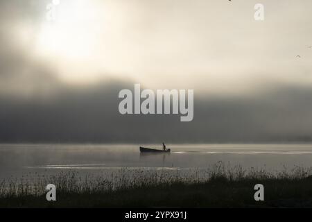 Beautiful scenery at Lac de Joux in the Swiss Jura mountains: A fisherman on his boat in the early morning, surrounded by fog on the calm water during Stock Photo