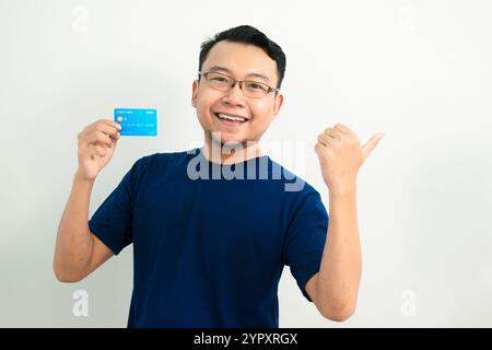 Happy asian man hold credit card with pointing pose. Banking, Financial isolated, blue color concept. Stock Photo