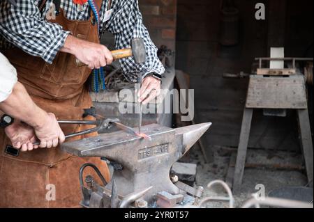 Photo of two blacksmiths hands working with hot metal making a tool on an iron anvil. Stock Photo