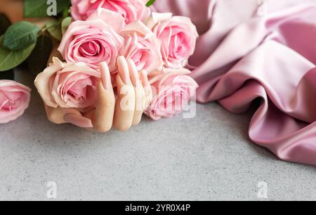 Woman's hand with perfect pink manicure is holding bunch of pink roses on grey table with pink silk fabric Stock Photo