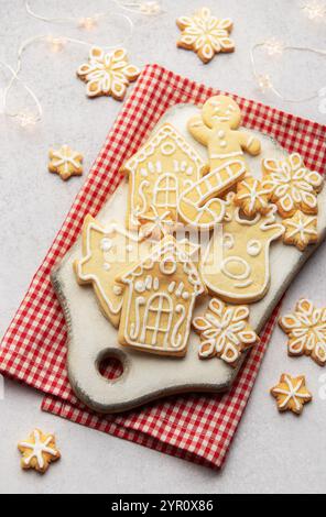 Delicious homemade christmas cookies shaped as snowflakes, gingerbread man, reindeer and houses lying on white cutting board on red checkered tableclo Stock Photo