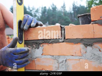 Bricklayer laying bricks and measuring brick wall with spirit level. Stock Photo