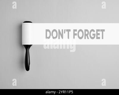 Don't forget reminder message. Lint roller with white trace on gray background with the message don't forget. Stock Photo