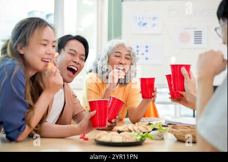 A group of joyful Asian diverse startup businesspeople celebrate in the office, laughing, chatting, and enjoying drinks. team building, corporate part Stock Photo