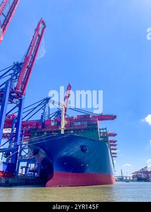 Massive cargo ship docked at a shipping terminal under a bright blue sky. High quality photo Stock Photo