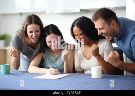 Excited interracial roommates signing lease contract in the kitchen at home Stock Photo
