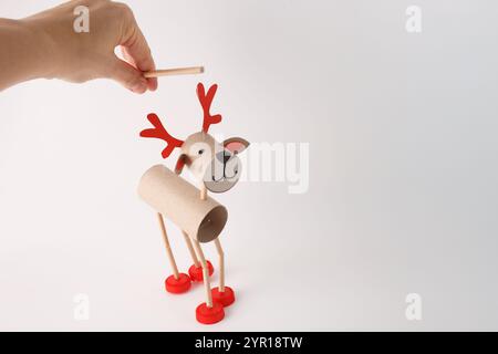 Hand holding DIY reindeer puppet made from cardboard tubes, red plastic caps, and paper details. Studio shot on a white background. Christmas craft an Stock Photo