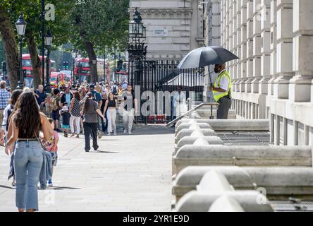 London, UK. Security guard with an umbrella standing outside the Cabinet Office on Whitehall on a sunny day. Stock Photo