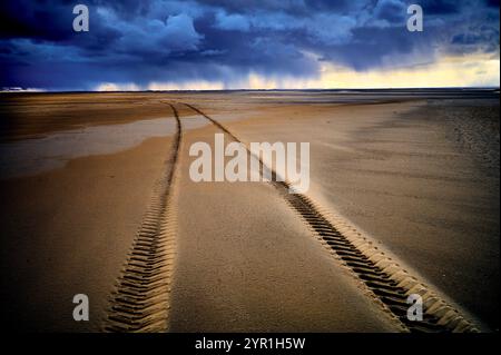 Tyre tracks on beach heading into a storm on the horizon Stock Photo