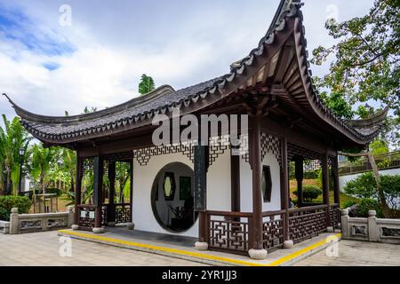 A white-walled Chinese pavilion with a curved roof and intricate lattice work details in Kowloon Walled City Park, Hong Kong. It features a round wind Stock Photo