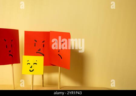 Horizontal image of yellow paper with smiling square face surrounded by angry square faces, concept of social rejection and discrimination with copy s Stock Photo