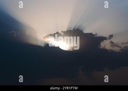 The sun's rays peek out from behind the gray clouds in the sky Stock Photo