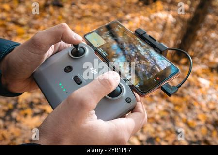 Kharkiv, Ukraine - October 15, 2021: Dji Mini (dji air) drone remote controller in operator hands. Flying drone close-up in autumn golden woods Stock Photo