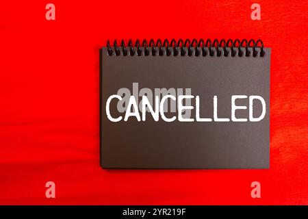 Cancelled message written on black notebook page with red background. Conceptual cancelled symbol. Copy space. Stock Photo