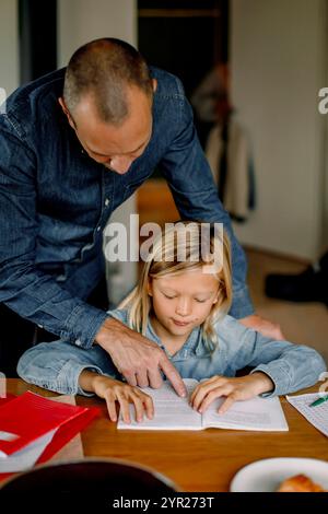 Father helping son doing homework while sitting near table at home Stock Photo