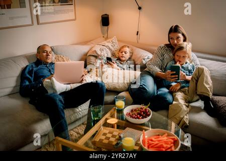 Family spending leisure time using wireless technologies while sitting on sofa at home Stock Photo