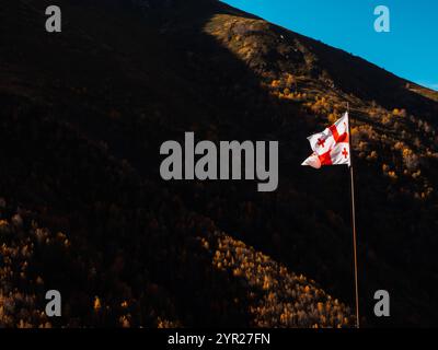 The national flag of Georgia fluttering in the wind on the pole, against autumn brown mountain and blue sky background with copy space. Stock Photo