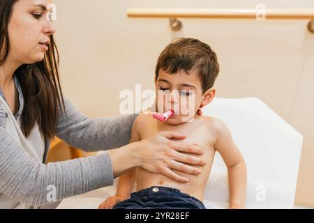 Physiotherapist helping child with respiratory physiotherapy using pink device Stock Photo