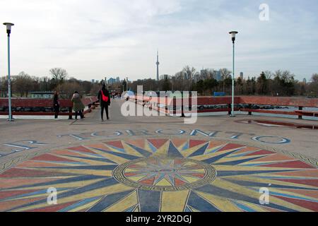 The observation deck on Centre Island Pier.  A male can be seen walking with a red fanny pack. A mosaic painted on the floor.  Downtown Toronto behind Stock Photo