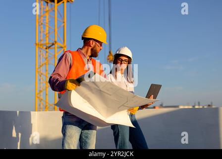 Construction workers reviewing blueprints on a building site with crane in the background, discussing project plans Stock Photo