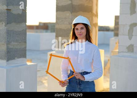 Confident female architect holding a folding ruler while inspecting a building under construction at sunset Stock Photo