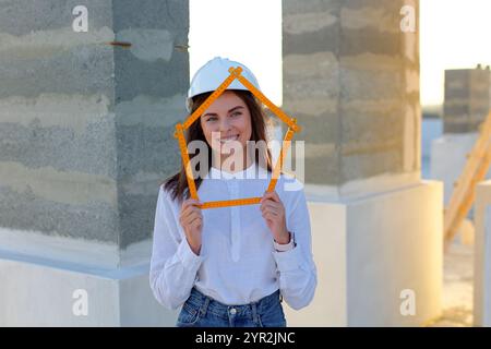 Confident female architect holding a folding ruler while inspecting a building under construction at sunset Stock Photo