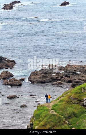 The treacherous rocky coastline at  Lizard Point with a young couple standing by cliff edge, most southerly point in England Cornwall UK Stock Photo