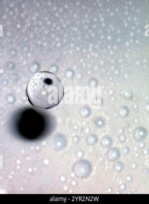 A clear sphere of water drop with a black shadow on it. The sphere is surrounded by many small white dots Stock Photo