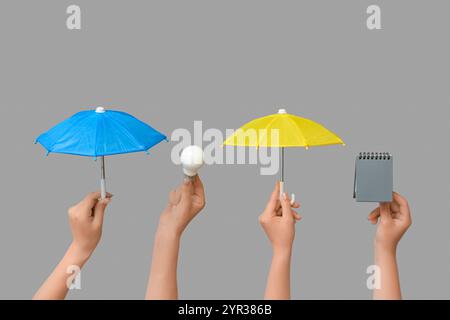 Female hands with different mini umbrellas, notebook and light bulb on grey background Stock Photo