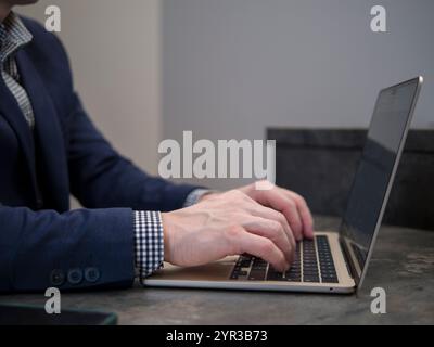 Professional businessman in modern office, typing on laptop while wearing suit and checkered shirt at his desk Stock Photo