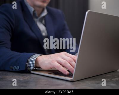Focused businessman in blue suit types on his laptop in professional office setting Stock Photo