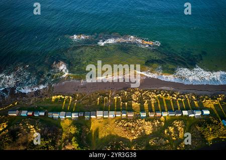 Hopeman Moray Coast Scotland sea breaking on rocks and sandy beach a row of coloured beach huts or chalets in winter sunshine Stock Photo
