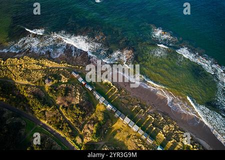 Hopeman Moray Coast Scotland the sea breaking on rocks and sand beach a row of beach huts or chalets in winter sunshine Stock Photo