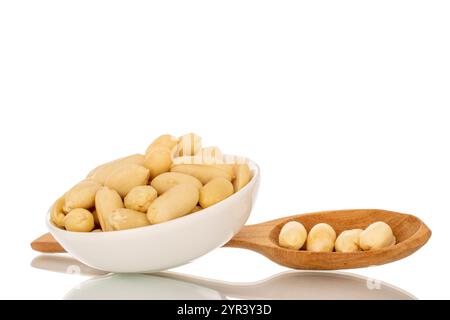 Roasted peanuts in a white ceramic saucer and with a wooden spoon, close-up, isolated on a white background. Stock Photo