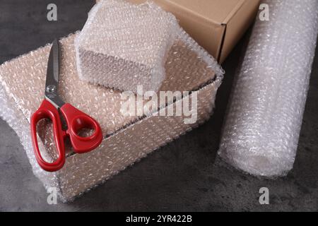 Cardboard boxes, bubble wrap and scissors on dark grey table Stock Photo