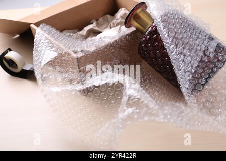 Beautiful glass vase in bubble wrap near cardboard box and adhesive tape on wooden table Stock Photo