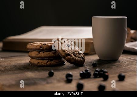 Home made Crispy Chocolate Cookies with Blueberries and Milk on Rustic Wooden table and Old Cook Book in the background Stock Photo