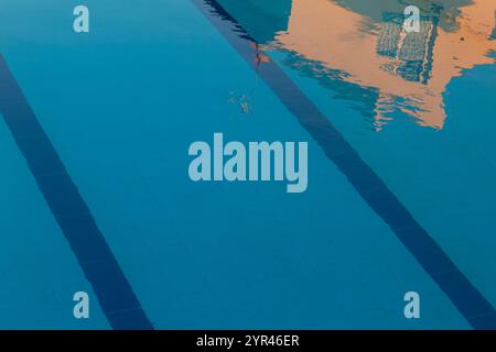 A vivid blue swimming pool surface, rippled with sunlight reflections, creates an intricate pattern of light and shadow. Stock Photo