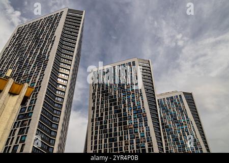 A modern architectural shot featuring three high-rise buildings with a geometric facade of glass windows under a partly cloudy sky, showcasing urban d Stock Photo