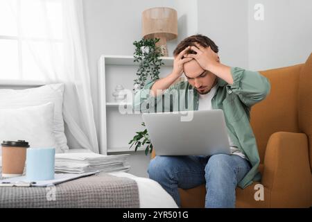 Stressed young man working with laptop in bedroom Stock Photo