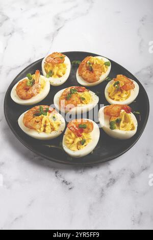 Boiled eggs stuffed with yolk and seasoned with mayonnaise, stuffed eggs with shrimp, on a black plate, selective focus, close-up, no people Stock Photo