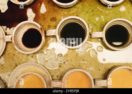 Dark coffee spots spread unevenly on the surface, the drops sparkle in the light, adding to the charm of the bar near the scattered cups. Stock Photo