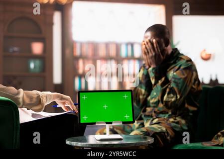 Black army soldier crying at therapy session next to chroma key screen, seeking professional support for PTSD and trauma recovery. Discussions for armed forces mental health care. Stock Photo