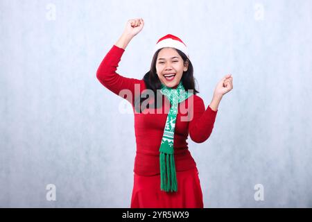 gesture Asian woman wearing red sweater party outfit with Santa hat and scarf, hands up dancing cheerful looking at camera, celebrating christmas and Stock Photo