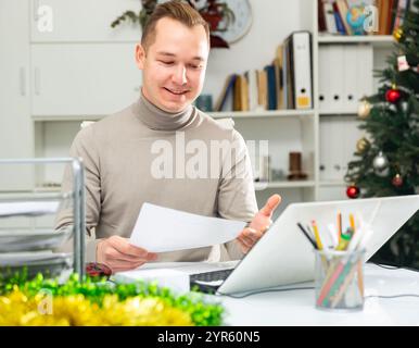 Positive man bookkeeper doing paperwork in office during Christmastime Stock Photo