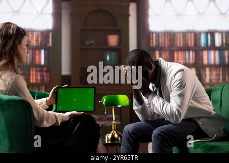 Black surgeon opening up about hard patient cases next to mockup display, psychologist listens in a therapy session. Physician crying and sharing feelings after losing people, trauma support. Stock Photo