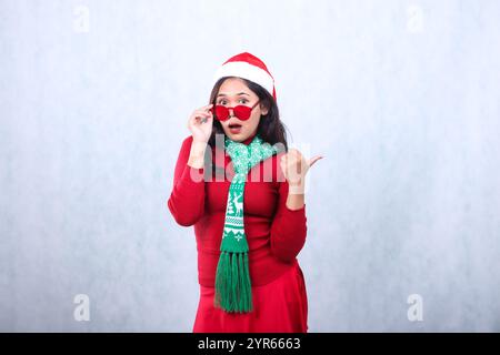 beautiful asian ladies wearing red sweater with Santa hat and scarf celebrating merry christmas, surprised to camera hand holding red glasses and poin Stock Photo